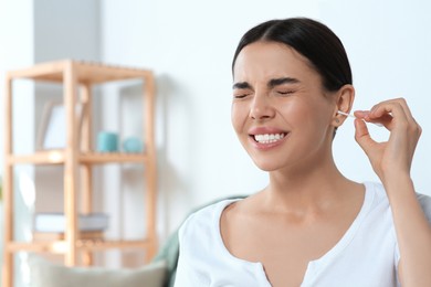 Young woman cleaning ear with cotton swab at home