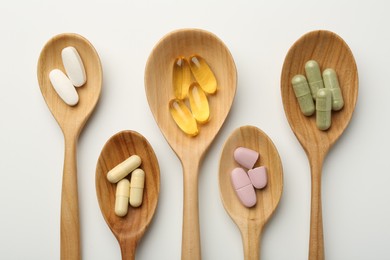 Photo of Vitamin capsules in wooden spoons on white background, flat lay