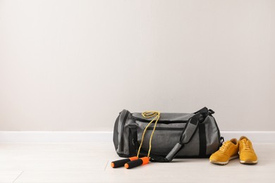 Photo of Grey bag and sports accessories on floor near light wall, space for text