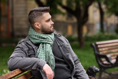 Photo of Handsome man in warm scarf on bench outdoors