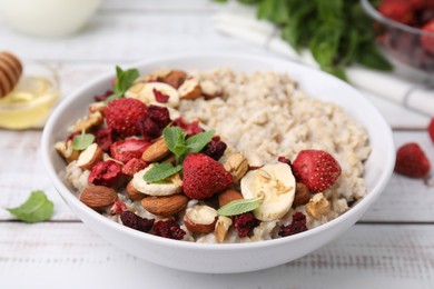 Photo of Delicious oatmeal with freeze dried berries, banana, nuts and mint on white wooden table, closeup