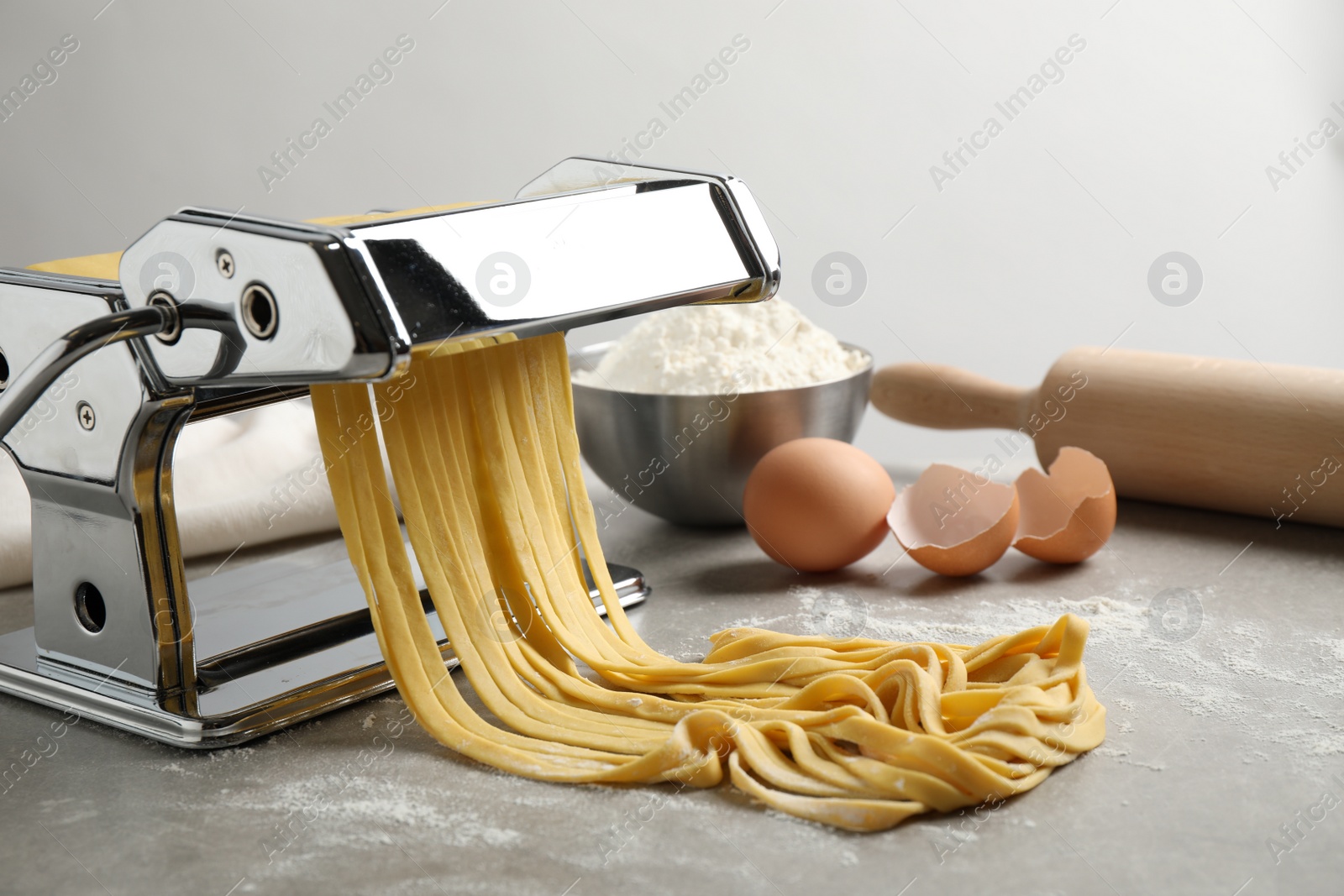 Photo of Pasta maker machine with dough and products on grey table