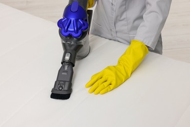 Photo of Woman in gloves disinfecting mattress with vacuum cleaner indoors, closeup