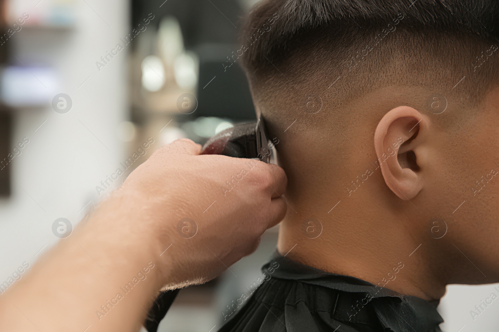 Photo of Professional barber making stylish haircut in salon, closeup