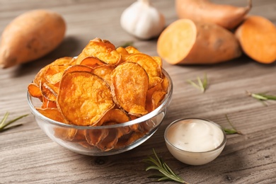 Photo of Delicious sweet potato chips in bowl, rosemary and sauce on table