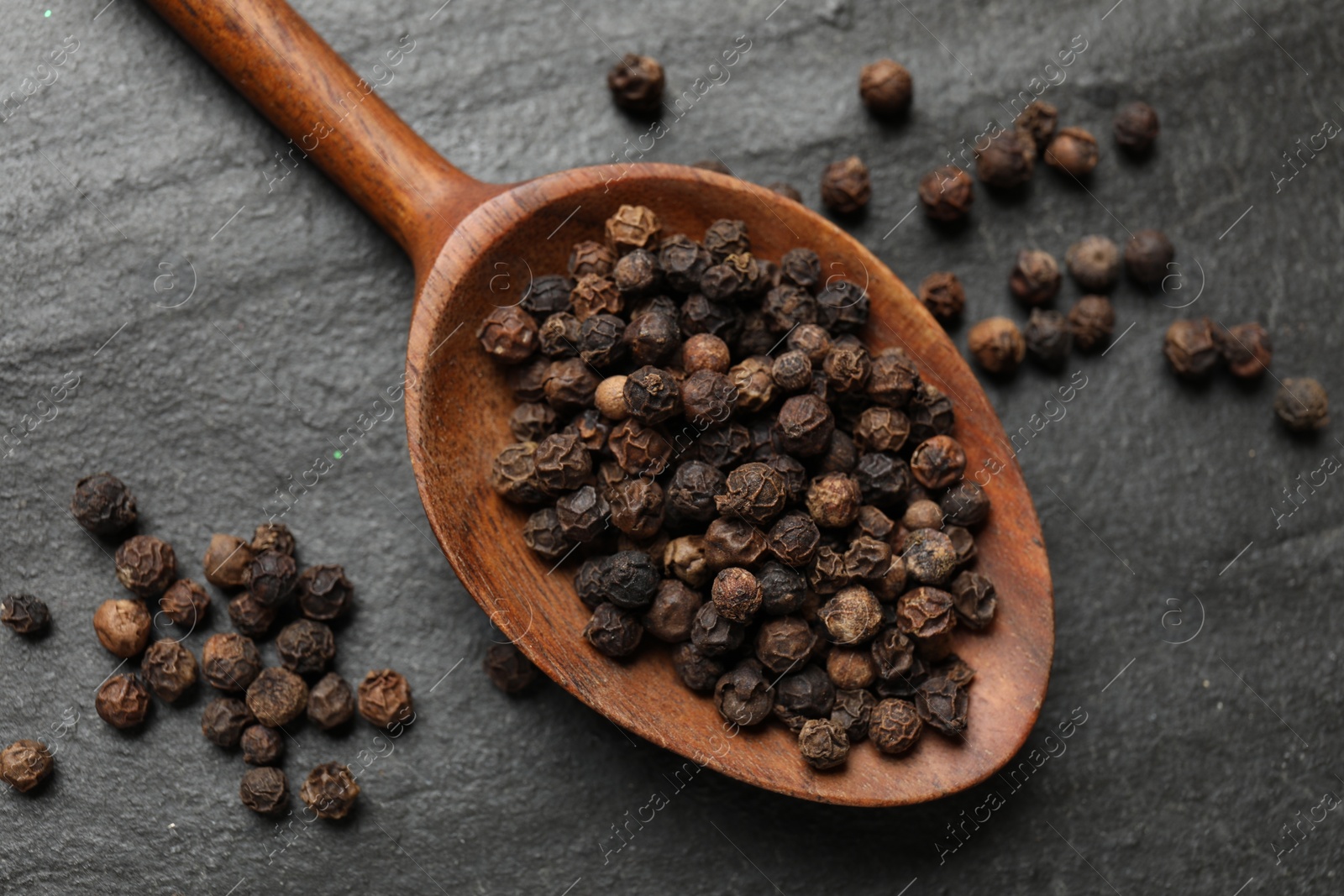 Photo of Aromatic spice. Pepper in spoon on black table, top view