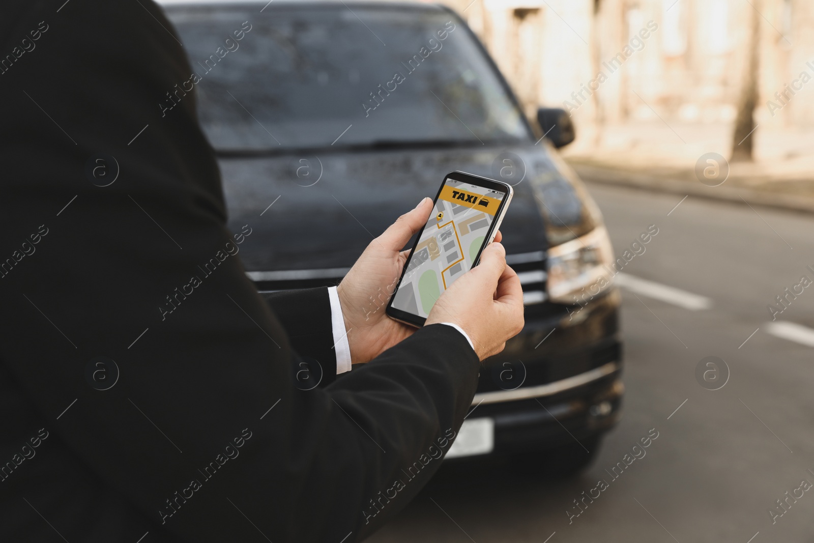 Photo of Businessman ordering taxi with smartphone on city street, closeup