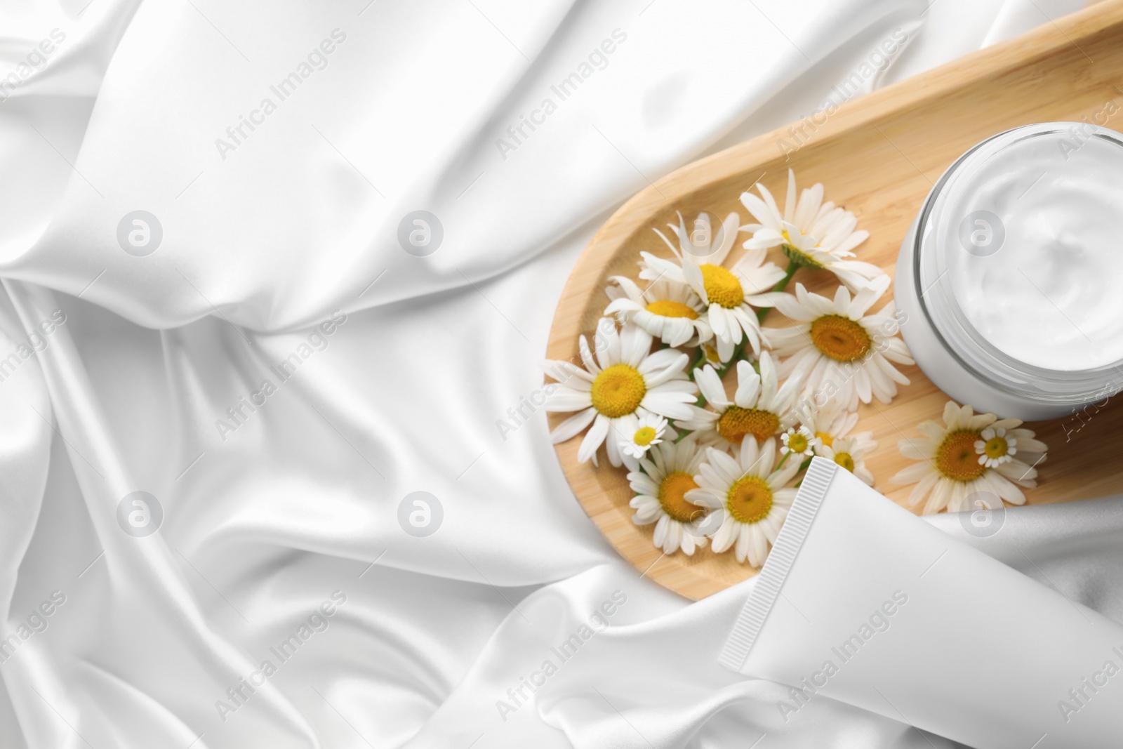 Photo of Different hand care cosmetic products and chamomiles on white silk fabric, flat lay. Space for text