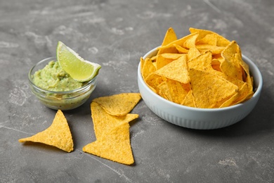 Photo of Delicious mexican nachos chips in bowl served with guacamole sauce and lime on grey table