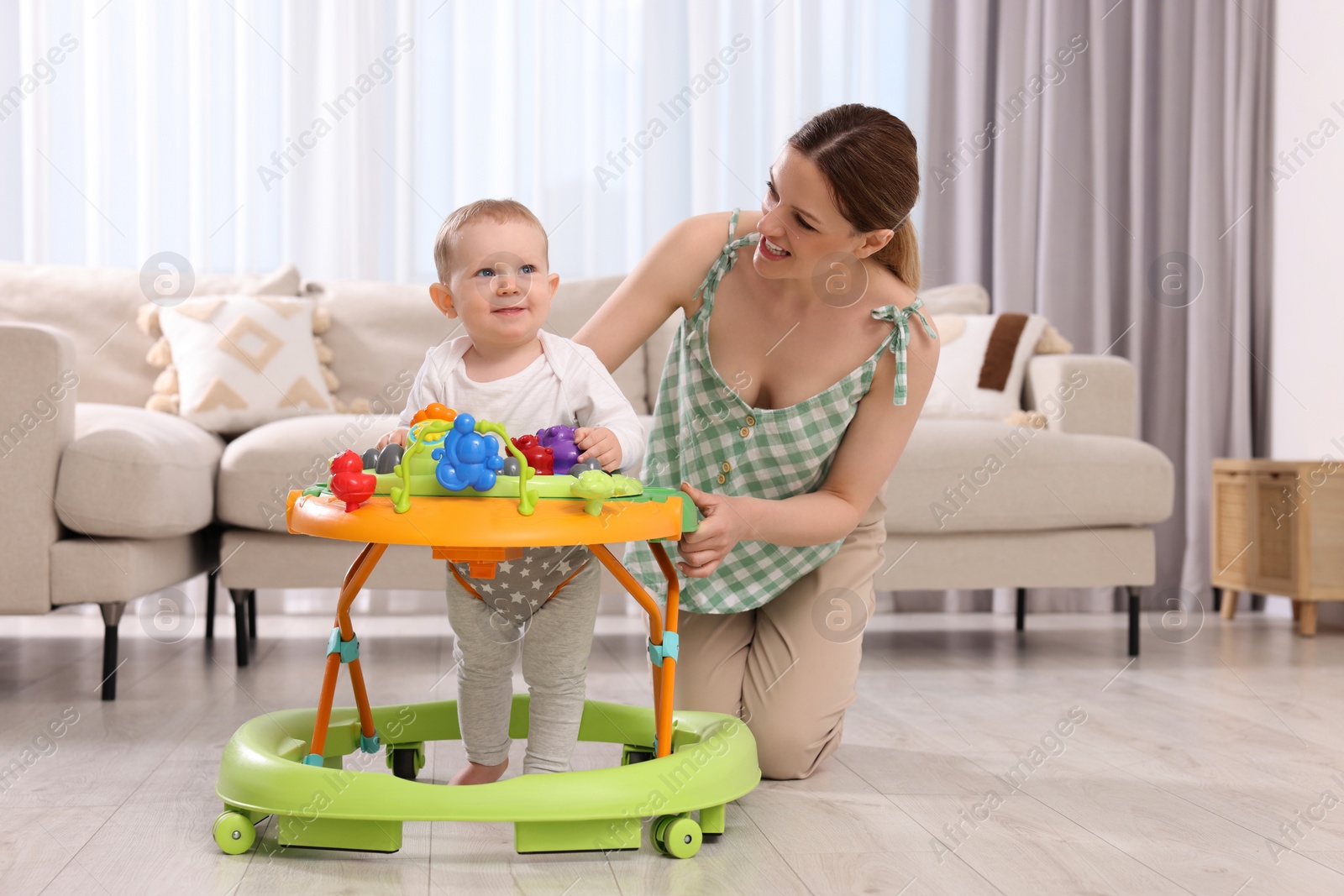 Photo of Cute boy making first steps with baby walker. Happy mother and her little son spending time together at home