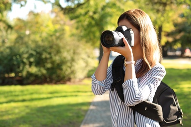 Photo of Young female photographer taking photo with professional camera in park. Space for text