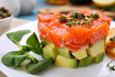 Delicious salmon tartare served with avocado on white plate, closeup