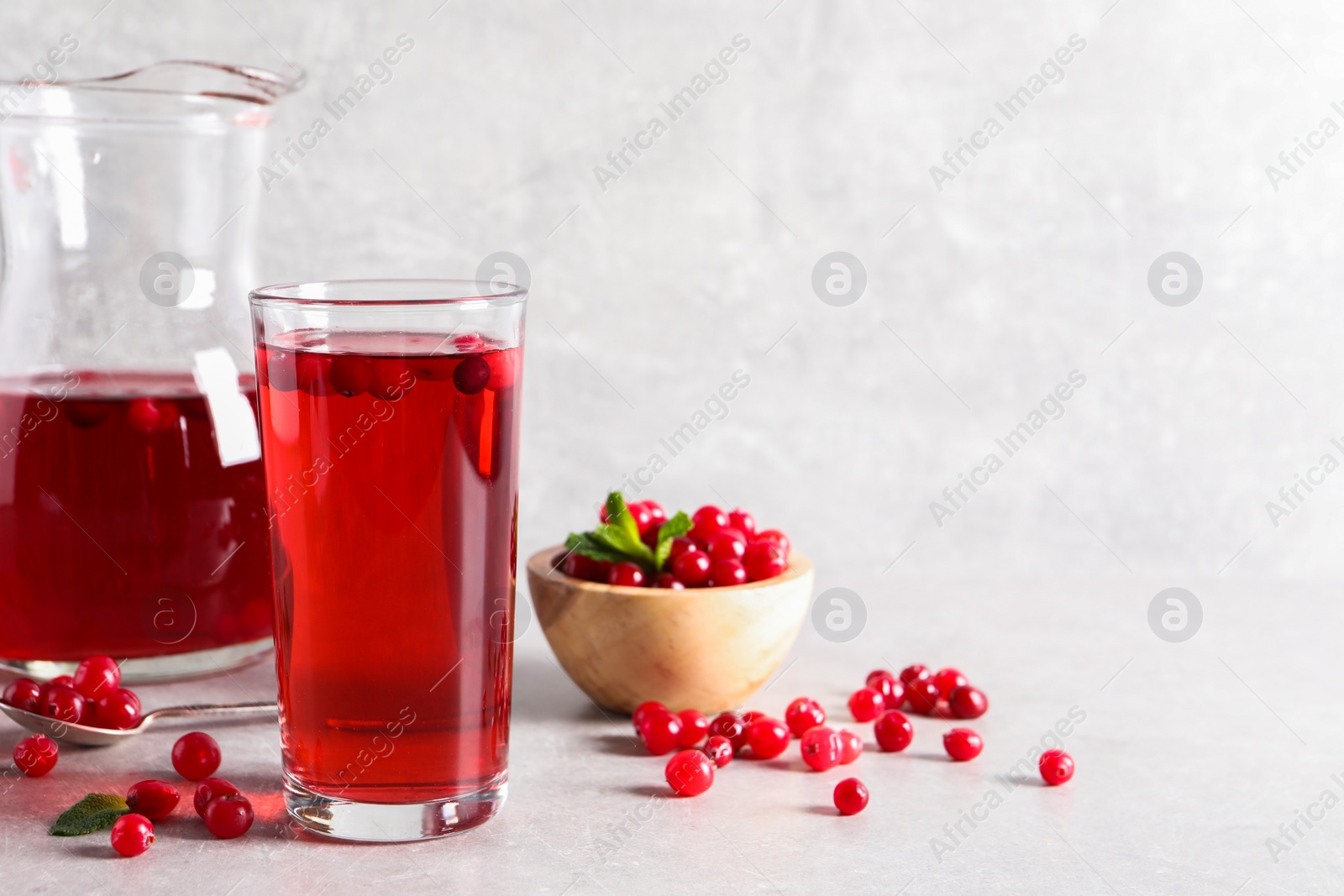 Photo of Tasty cranberry juice in glass and fresh berries on light grey table, space for text