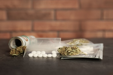 Plastic bags with pills, hemp buds and money on grey table