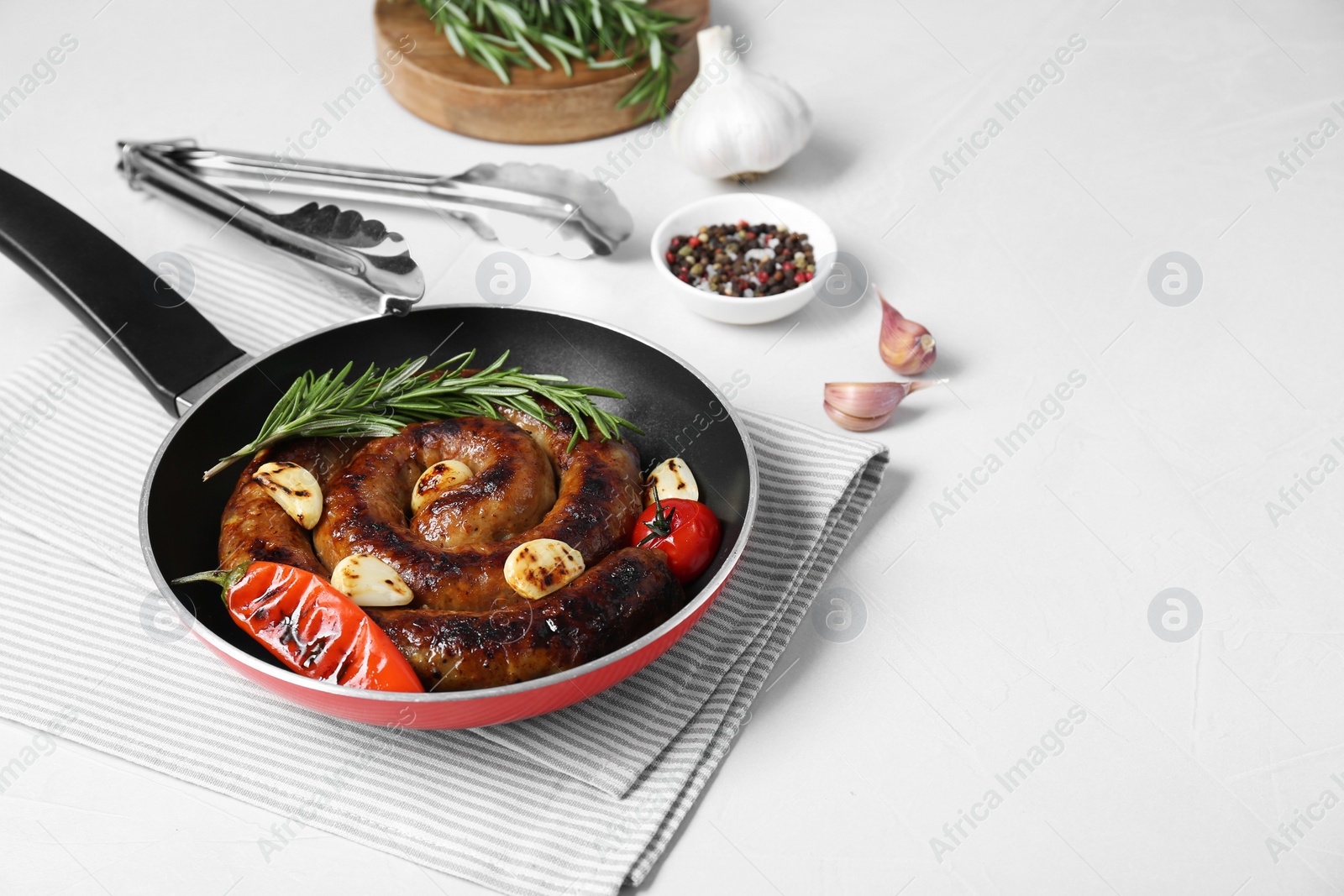 Photo of Delicious homemade sausage with garlic, tomato, rosemary and chili in frying pan on white table. Space for text