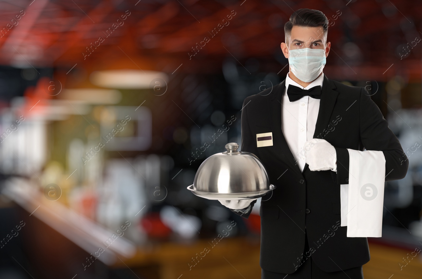 Image of Waiter in medical face mask holding tray with lid in restaurant