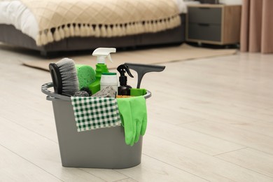 Photo of Different cleaning supplies in bucket on floor at home, space for text