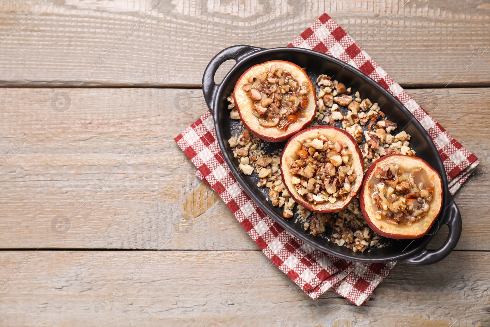 Photo of Tasty baked apples with nuts and honey in baking dish on wooden table, top view. Space for text