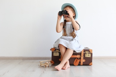 Photo of Adorable little child playing traveler with suitcase indoors