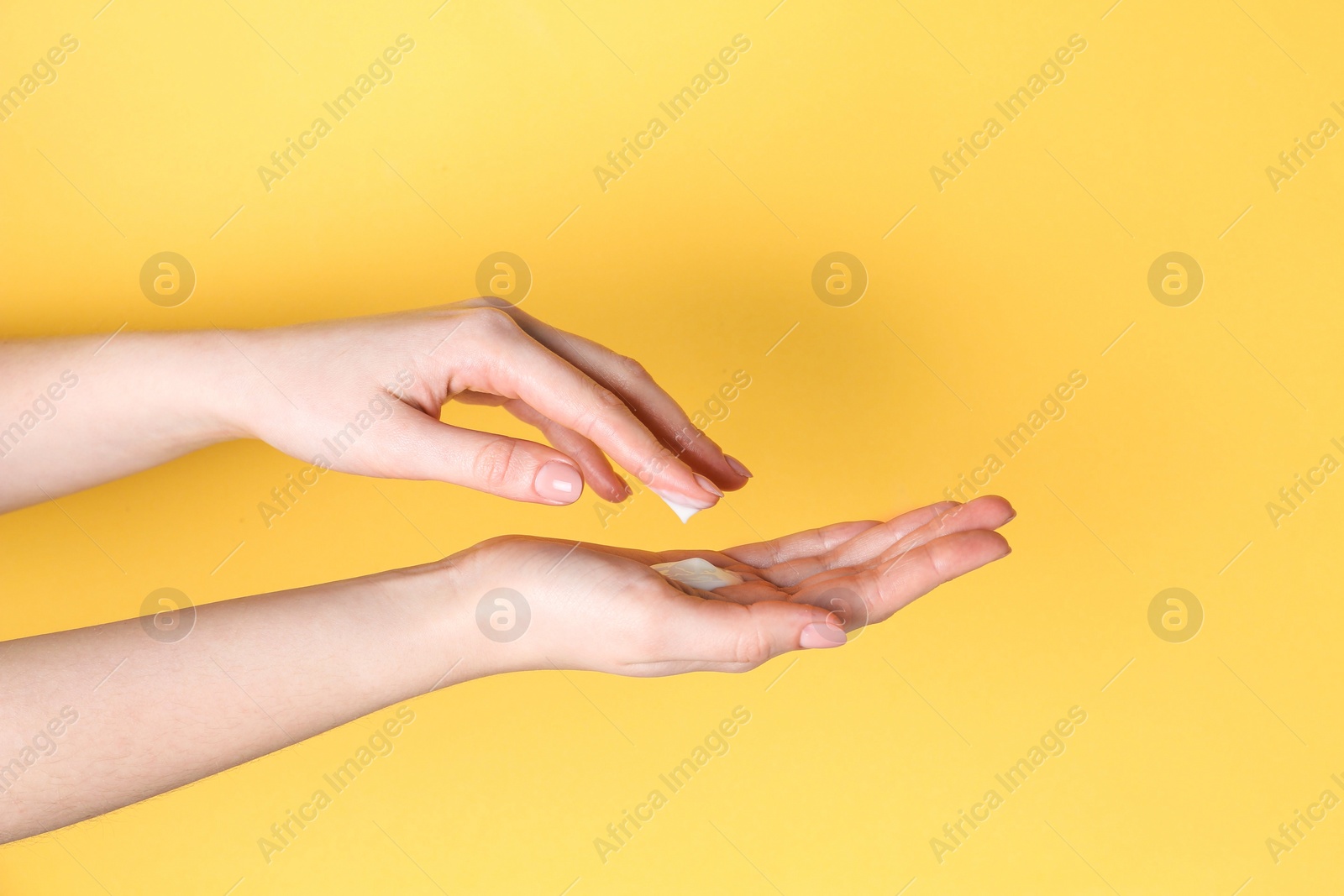 Photo of Woman applying cream on her hand against yellow background, closeup