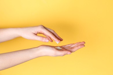 Photo of Woman applying cream on her hand against yellow background, closeup