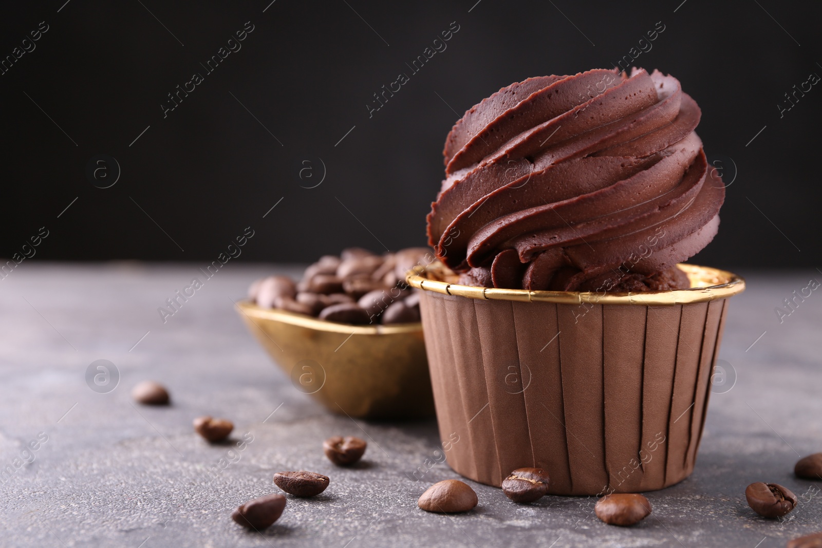 Photo of Delicious chocolate cupcake and coffee beans on grey textured table, closeup. Space for text