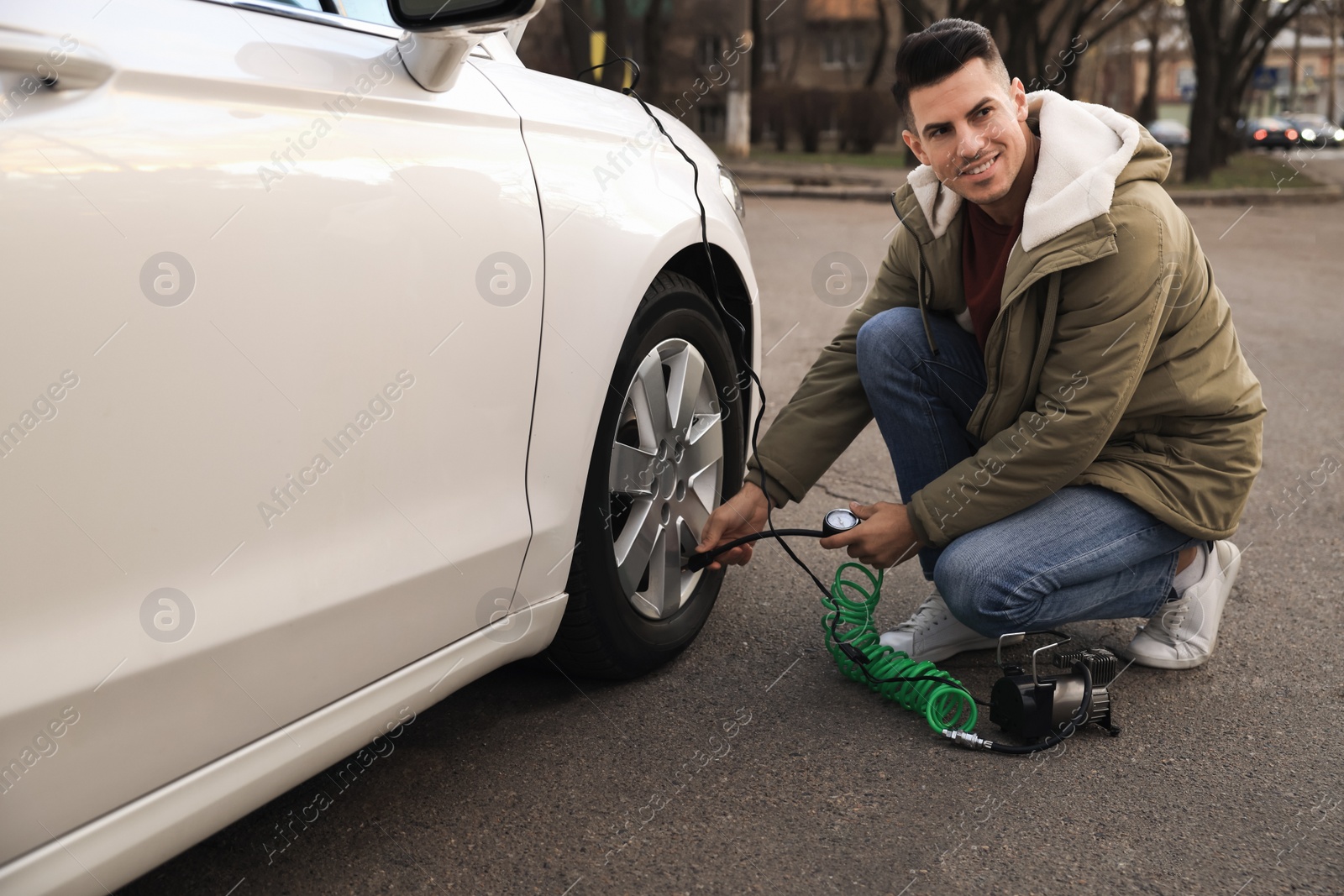 Photo of Handsome man inflating car tire with air compressor on street