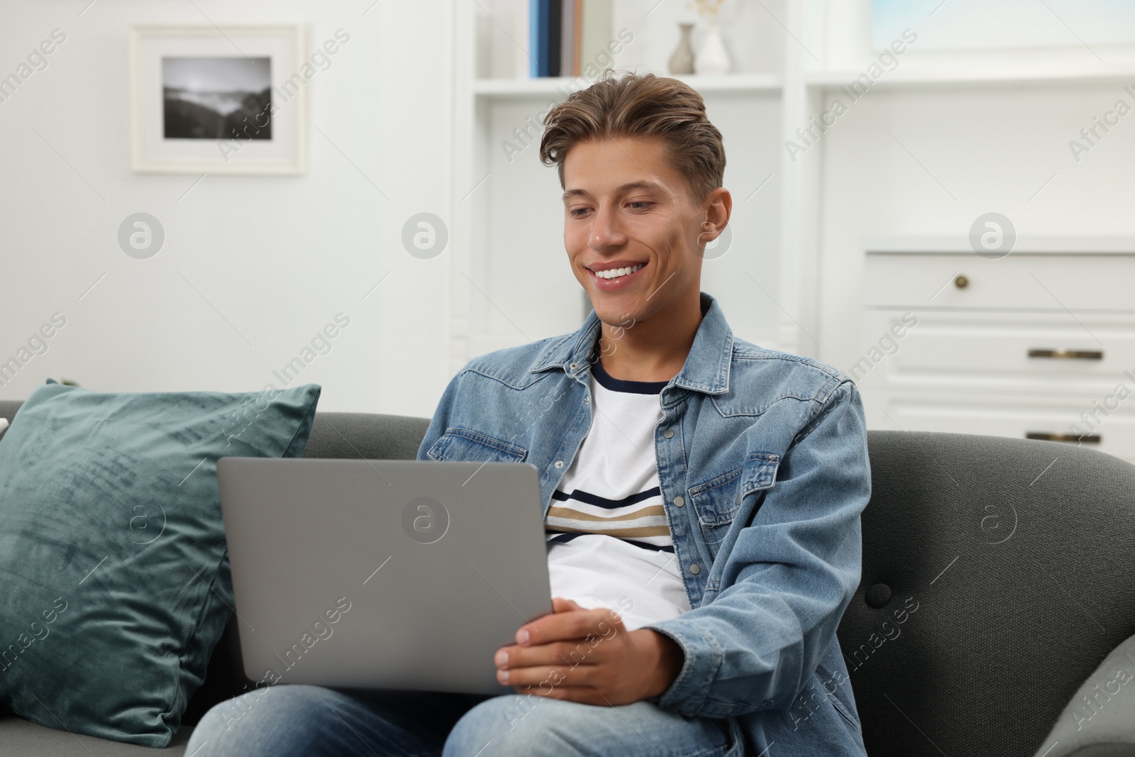 Photo of Happy young man having video chat via laptop on sofa indoors