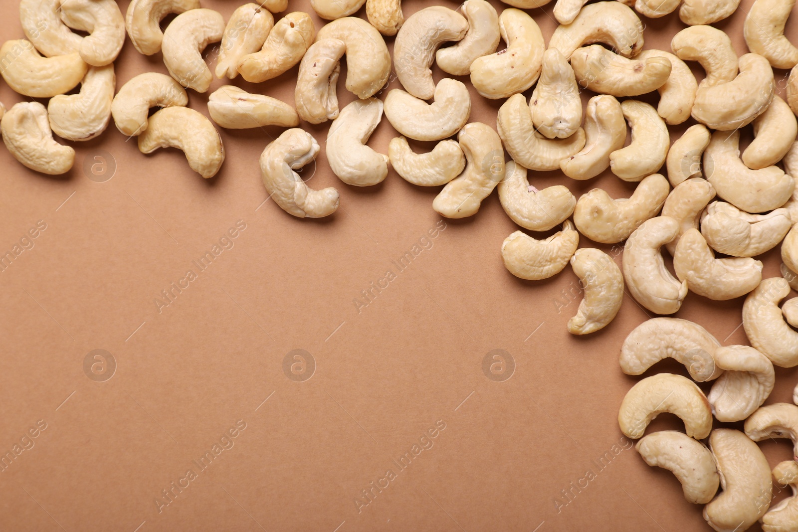 Photo of Many tasty cashew nuts on pale brown background, top view. Space for text