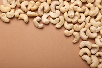 Many tasty cashew nuts on pale brown background, top view. Space for text