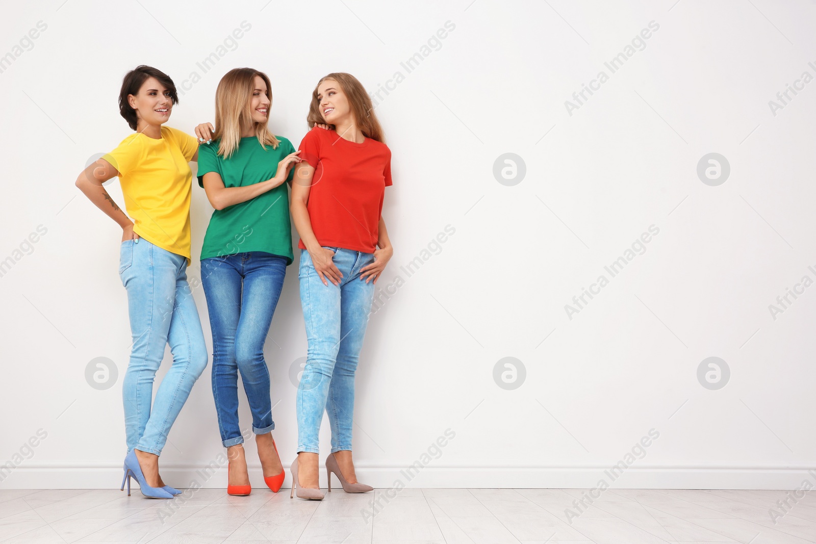 Photo of Group of young women in jeans and colorful t-shirts near light wall