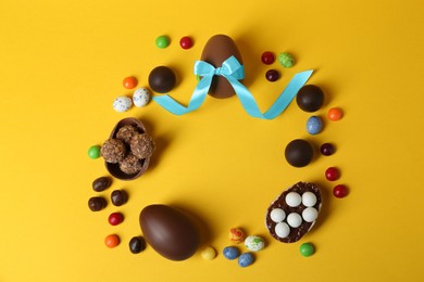 Photo of Frame of chocolate eggs and candies on yellow background, flat lay. Space for text
