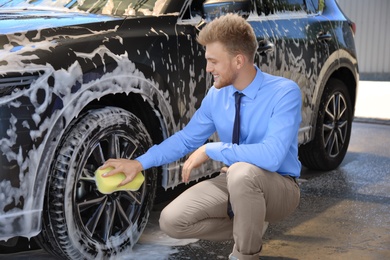 Businessman cleaning auto with sponge at self-service car wash