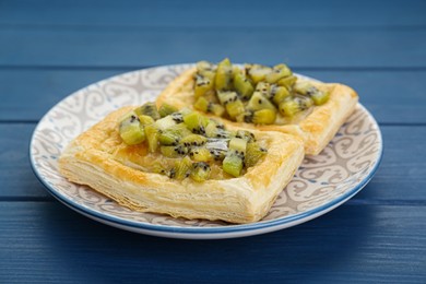 Photo of Fresh tasty puff pastry with kiwi on blue wooden table, closeup