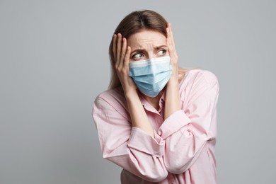 Young woman in protective mask feeling fear on grey background