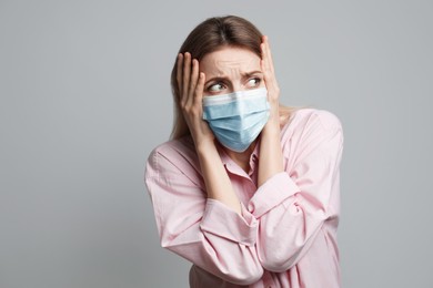 Photo of Young woman in protective mask feeling fear on grey background