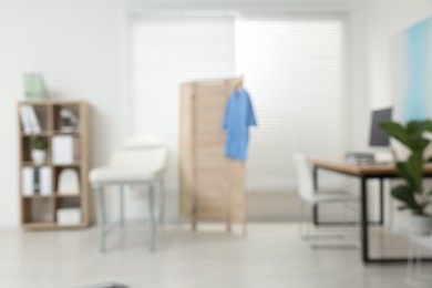 Photo of Blurred view of modern medical office with doctor's workplace and examination table in clinic