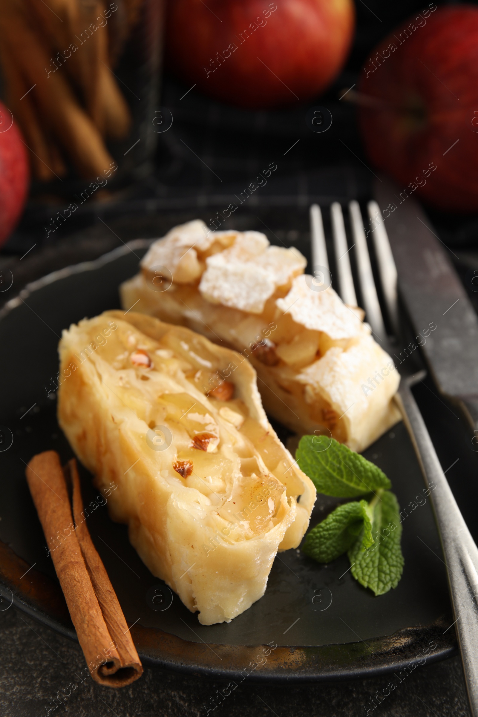 Photo of Delicious apple strudel with almonds, cinnamon and mint on plate, closeup