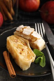 Photo of Delicious apple strudel with almonds, cinnamon and mint on plate, closeup