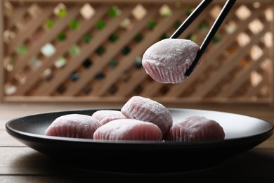 Photo of Taking delicious mochi from plate with chopsticks on wooden table. Traditional Japanese dessert