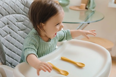 Photo of Cute little baby sitting in high chair indoors