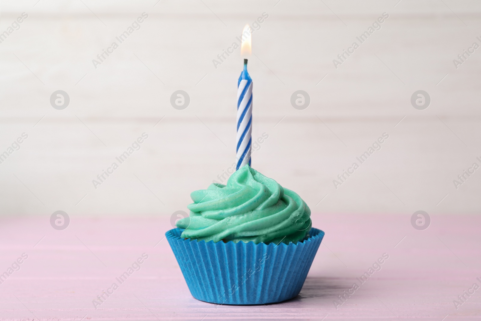 Photo of Delicious birthday cupcake with cream and burning candle on pink table