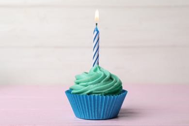 Delicious birthday cupcake with cream and burning candle on pink table