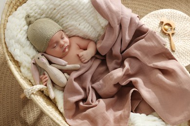 Photo of Cute newborn baby with toy bunny sleeping in cradle at home, top view
