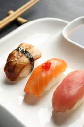 Plate with delicious nigiri sushi and soy sauce on black table, closeup
