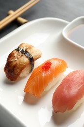 Photo of Plate with delicious nigiri sushi and soy sauce on black table, closeup