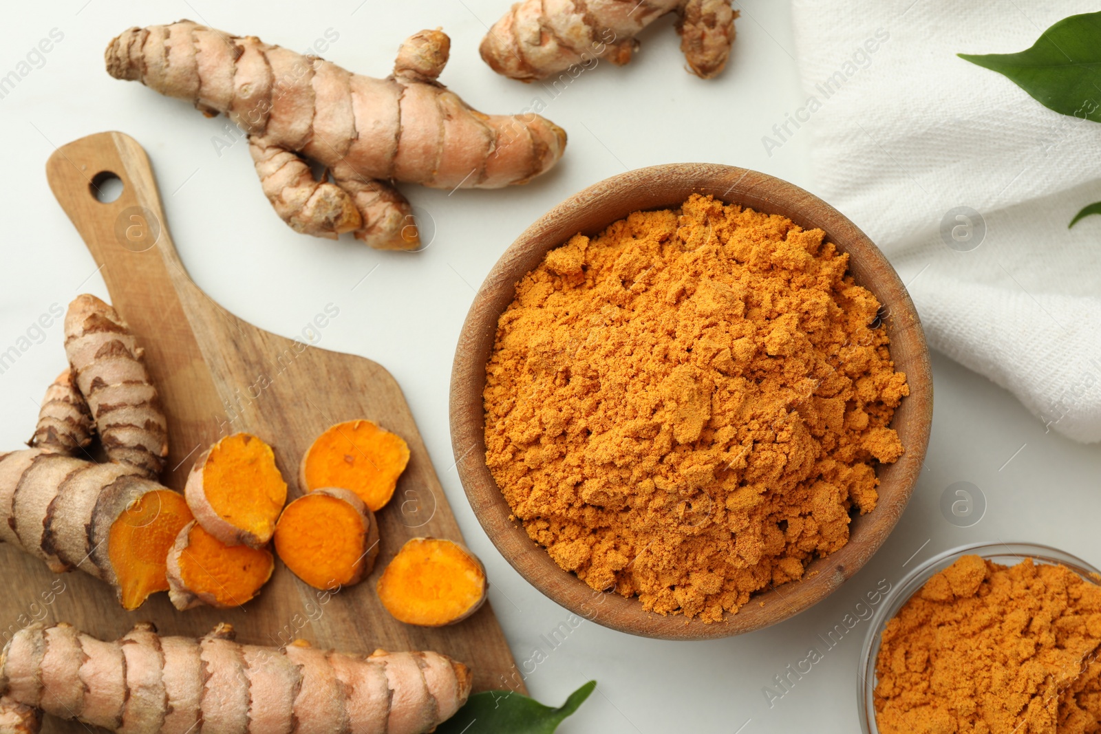 Photo of Aromatic turmeric powder and raw roots on white table, flat lay