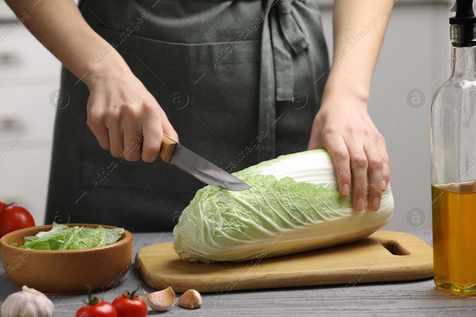 Photo of Woman cutting fresh chinese cabbage at grey wooden table in kitchen, closeup