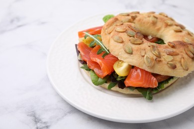 Photo of Tasty bagel with salmon and tomatoes on white marble table, closeup. Space for text