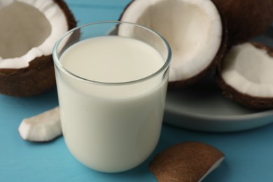 Glass of delicious vegan milk and coconuts on light blue wooden table, closeup